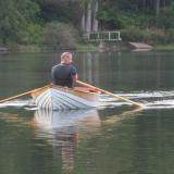 Port bow view of Michael rowing his boat on a calm lake.