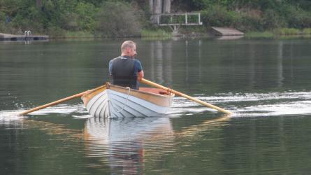 Port bow view of Michael rowing his boat on a calm lake.