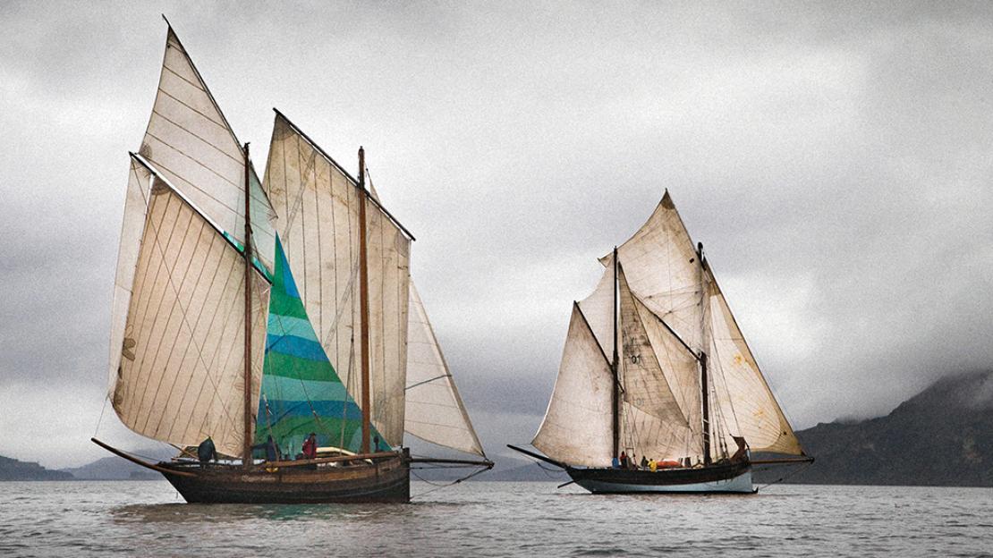 Two wooden sailboats on the water under a cloudy sky.