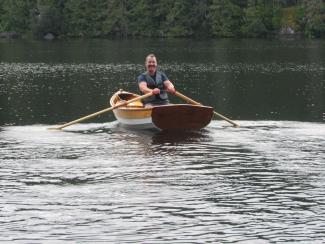 Port quarter view of Michael rowing his boat on a calm lake